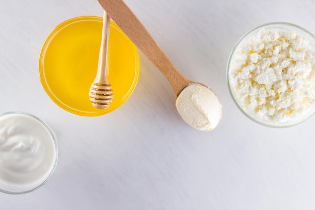Hüttenkäse-Joghurt und Sauerrahm auf weißem Hintergrund Milchprodukte und Honig mit Holzbesteck aus nächster Nähe
