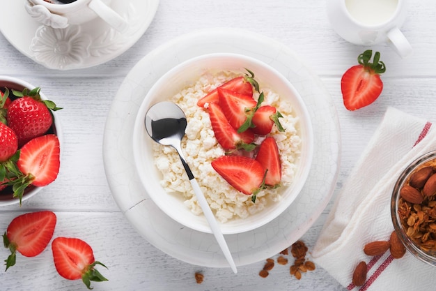 Hüttenkäse mit Erdbeeren Frühstück aus Hüttenkäse mit Scheiben frischen Erdbeeren Sahnetasse Kaffee in weißer Schüssel auf weißem Holzhintergrund Ansicht von oben Lebensmittelkonzept Mock up