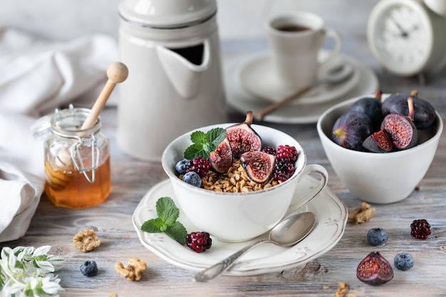 Hüttenkäse mit Feigen, Beeren, Honig. Tasse Kaffee und Kaffeekanne. Frühstück. Holztisch.