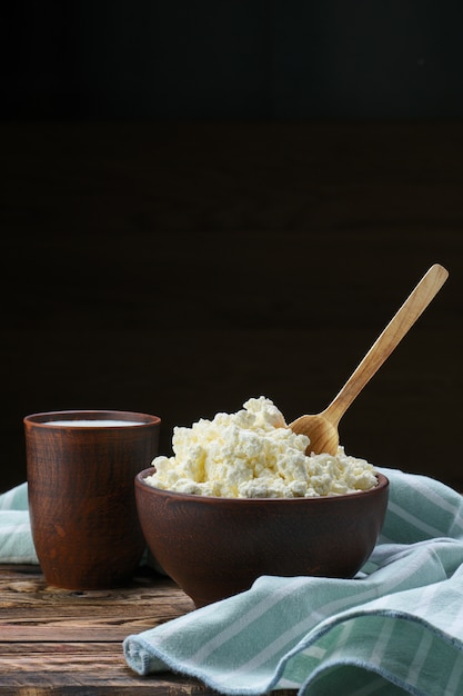 Hüttenkäse mit hölzernem löffel in ihm und milch in den tonwaren auf holztisch