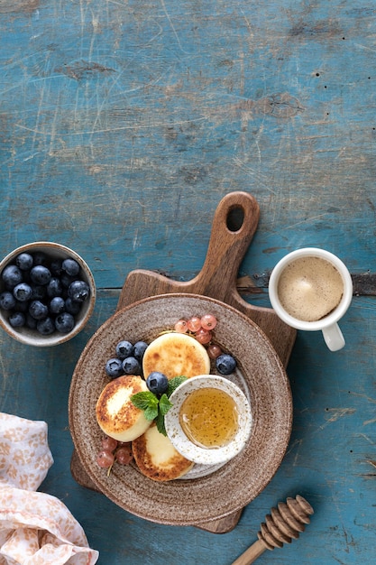 Hüttenkäse-Pfannkuchen Käsekuchen Ricotta Krapfen mit frischen Heidelbeeren, Johannisbeeren und Pfirsiche auf einem Teller Gesundes und leckeres Frühstück für den Urlaub Blauer Hintergrund aus Holz