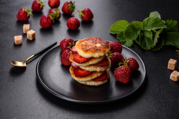 Hüttenkäse-Pfannkuchen mit geschnittenen Erdbeeren und Erdbeermarmelade auf einem Teller auf Betongrund