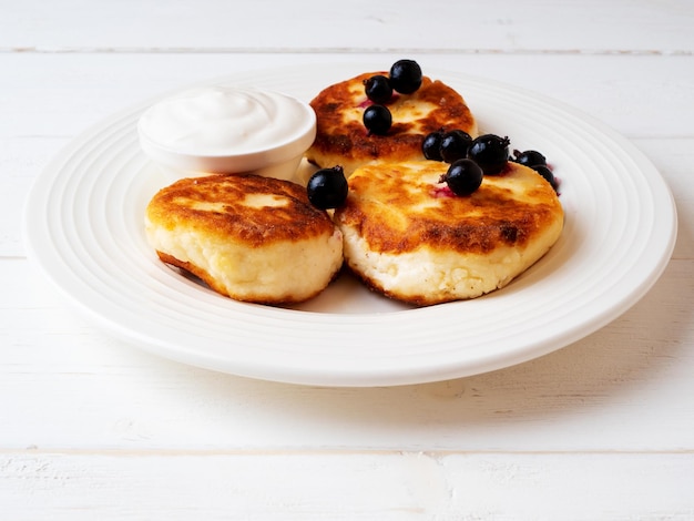 Hüttenkäse-Pfannkuchen mit Sauerrahm und schwarzer Johannisbeere auf einer weißen Keramikplatte Frühstückskonzept
