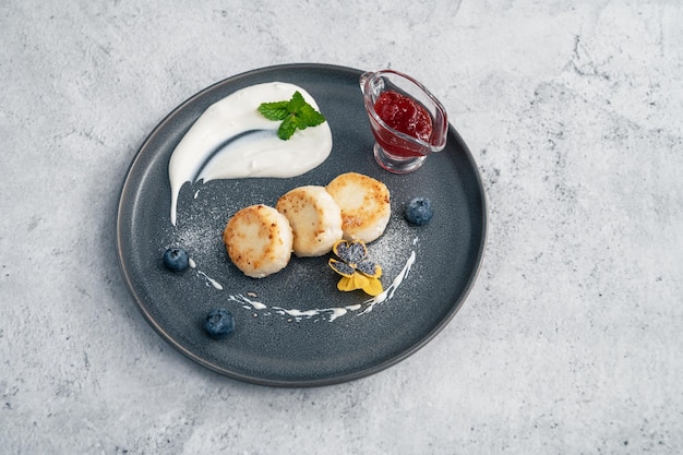 Hüttenkäse-Pfannkuchen Syrniki auf Teller mit Sauerrahm und Marmelade Blaubeere und essbare Blumen Gesundheit