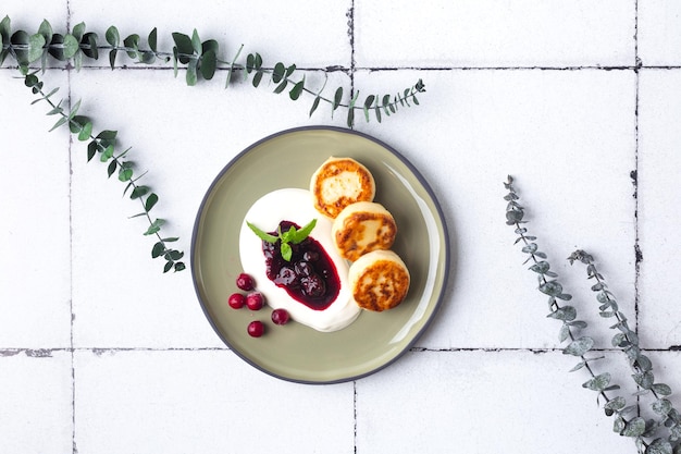 Hüttenkäse-Pfannkuchen Syrniki mit frischen Beeren und Marmelade zum Frühstück auf Fliesen mit Eukalyptus...