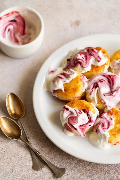 Hüttenkäse-Pfannkuchen Syrniki Ricotta-Krapfen auf weißer Keramikplatte mit Sauerrahm und Marmelade Gesundes und leckeres Frühstück am Morgen Beige Hintergrund Essen für Kinder