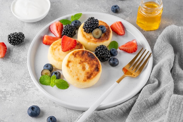 Hüttenkäse-Pfannkuchen Syrniki-Ricotta-Krapfen mit frischem Beerenhonig und Sauerrahm