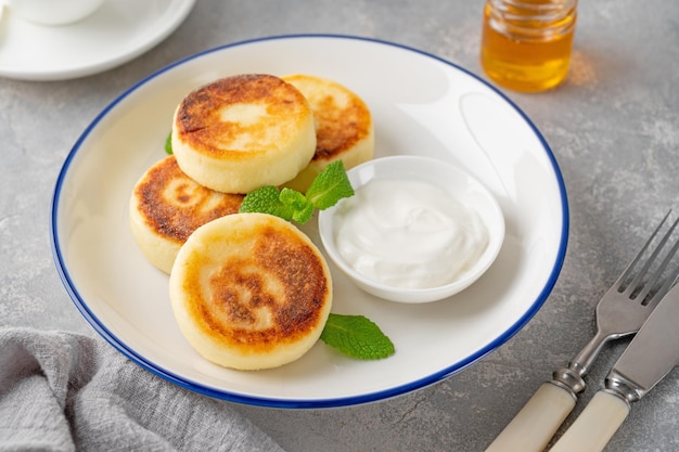 Hüttenkäse-Pfannkuchen Syrniki Ricotta Krapfen mit Honig und Sauerrahm Gesundes Frühstück