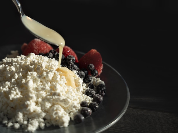 Hüttenkäse wird auf einem schwarzen Teller mit gekühlten Beeren und Kondensmilch serviert