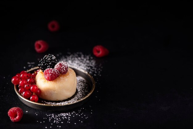 Hüttenkäsepfannkuchen mit Beeren und Puderzucker auf einem schwarzen Teller