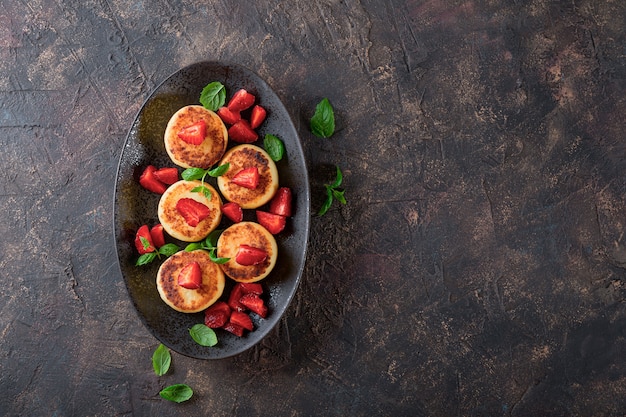 Hüttenkäsepfannkuchen mit Erdbeeren und Minze auf einem Draufsichtfoto der schwarzen Platte mit freiem Speicherplatz