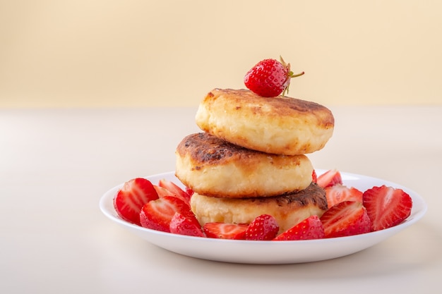 Hüttenkäsepfannkuchen mit geschnittenen Erdbeeren auf weißer Platte lokalisierten Winkelsicht