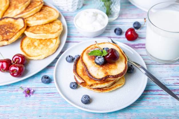 Hüttenkäsepfannkuchen (Syrniki). Hausgemachte Käsekuchen aus Hüttenkäse mit Sauerrahm, Beeren und Milch. Traditionelles russisches Gericht. Nahansicht.