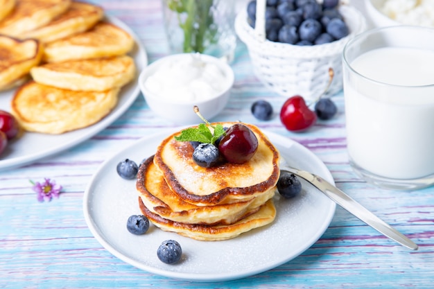 Hüttenkäsepfannkuchen (syrniki). hausgemachte käsekuchen aus hüttenkäse mit sauerrahm, beeren und milch. traditionelles russisches gericht. nahansicht.