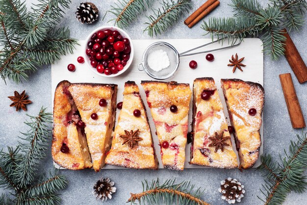 Hüttenkäsetortenauflauf mit den Moosbeeren und Gewürzen besprüht mit Puderzucker auf einem hölzernen Stand. Grauer Betontisch.