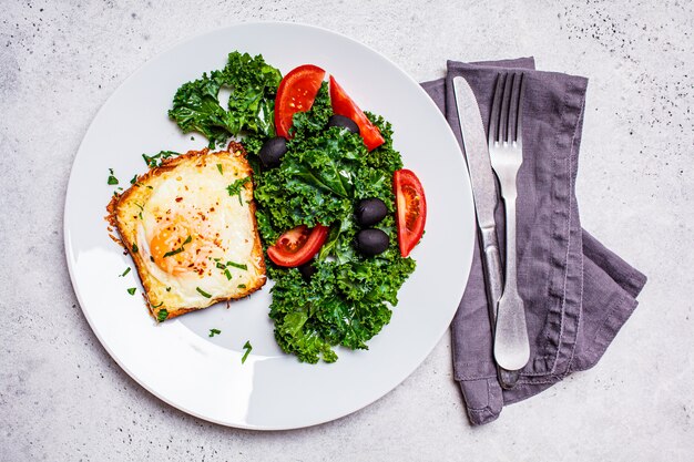 Huevo al horno con tostadas de queso y ensalada en una placa blanca.