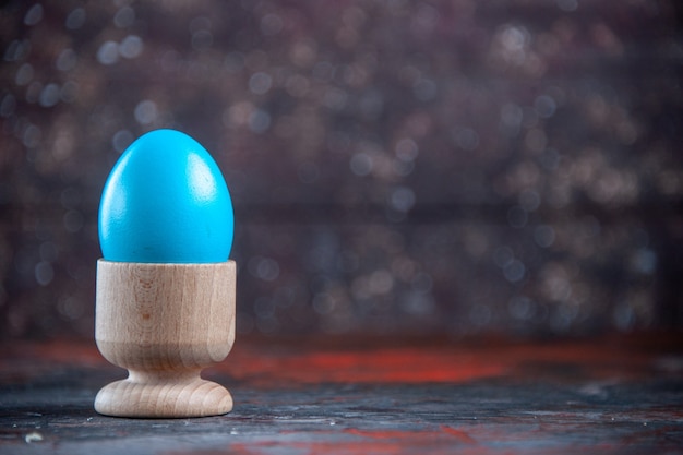 Huevo azul claro en un recipiente marrón en el lado derecho sobre fondo angustiado de colores oscuros con espacio libre