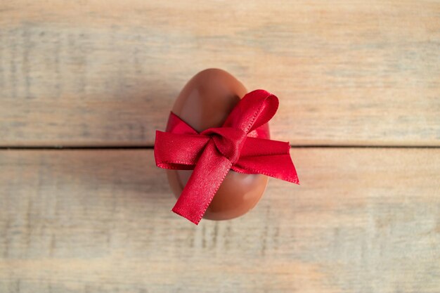 Huevo de chocolate con cinta de seda roja en un fondo de madera