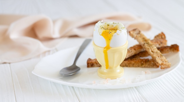 Huevo cocido en un plato blanco con tostadas y cuchara para el desayuno