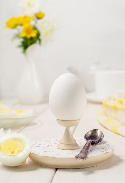 Huevo cocido en un soporte de cerca sobre un fondo de madera blanca. Foto de comida en clave de luz.