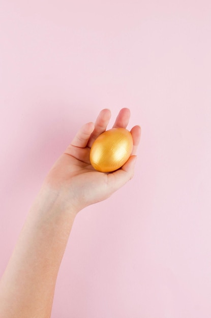 Huevo de color dorado en mano sobre fondo rosa pastel Concepto de Pascua mínimo Tarjeta de Pascua feliz