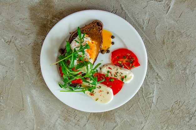 huevo escalfado sobre pan negro con tomate mozzarella y rúcula