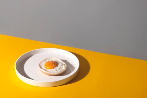 Huevo frito en plato blanco sobre amarillo con sombras.