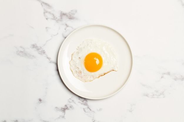 Foto un huevo frito en un plato blanco sobre una mesa de mármol