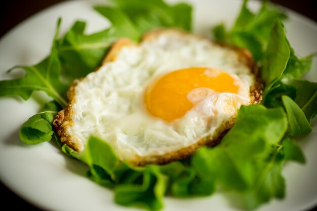 Un huevo frito con rúcula y lechuga en un plato sobre una mesa de madera