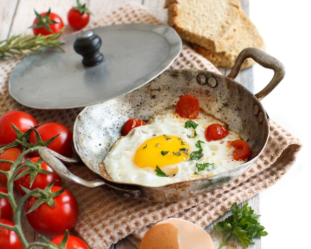 Huevo frito con tomate, pan casero y hierbas en una vieja sartén de madera de cerca