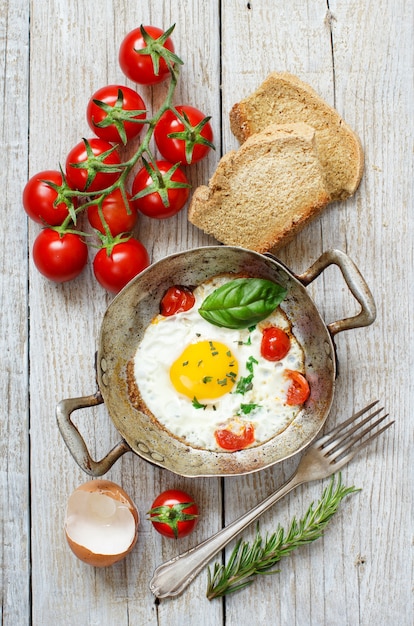 Huevo frito con tomates, pan casero y hierbas en una vieja sartén en la vista superior de madera