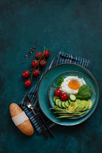 Huevo frito con las verduras frescas y el pan en fondo verde concreto.