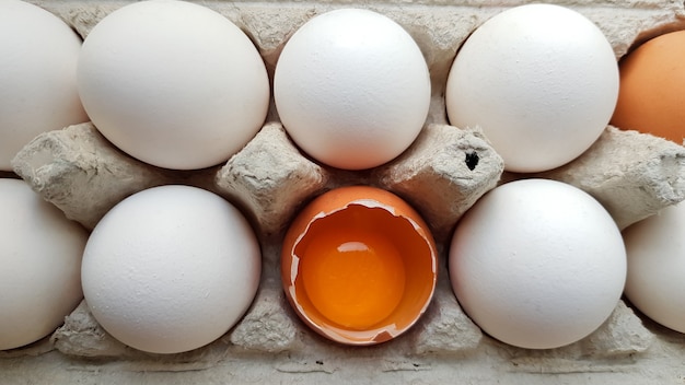 Un huevo de gallina está medio roto entre otros huevos. Primeros planos en una bandeja de papel para almacenamiento.