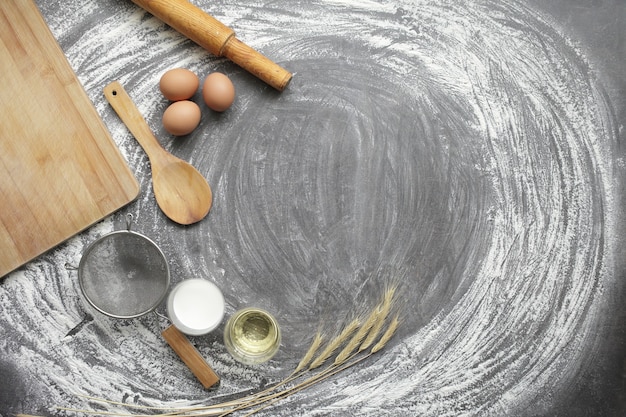 Huevo de gallina, harina, aceite de oliva, leche, espigas, herramienta de cocina en el fondo de la tabla gris.