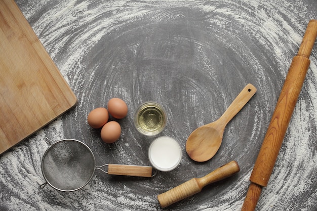 Huevo de gallina, harina, aceite de oliva, leche, herramienta de cocina sobre fondo gris de la tabla.