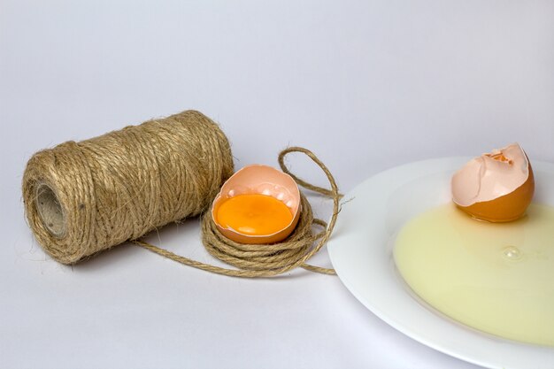 Huevo de gallina roto en hilo decorativo en blanco