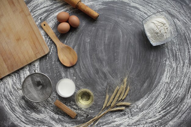 Huevo, harina, aceite de oliva, leche, espigas de trigo, herramienta de cocina sobre fondo de mesa gris.