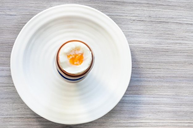 Huevo marrón pasado por agua en una taza en un plato en gris