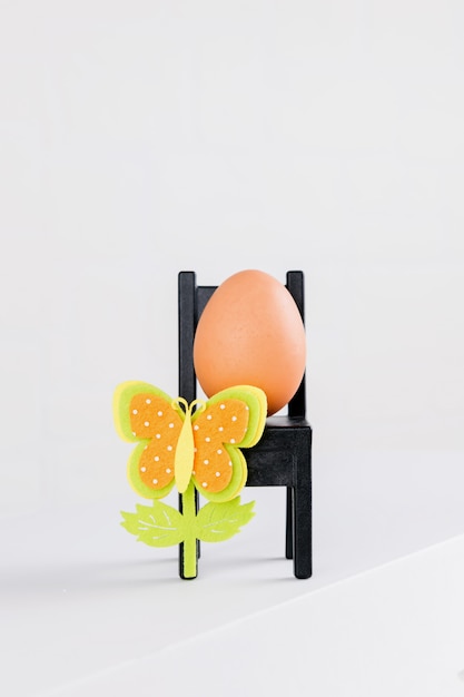 Un huevo natural está sentado en una silla negra con decoración de flores de pascua. minimale idea del concepto de pascua.
