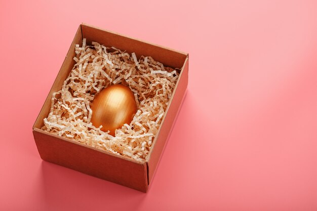 Huevo de oro en una caja de madera sobre un fondo rosa. El concepto de exclusividad y superprecio. Composición minimalista.