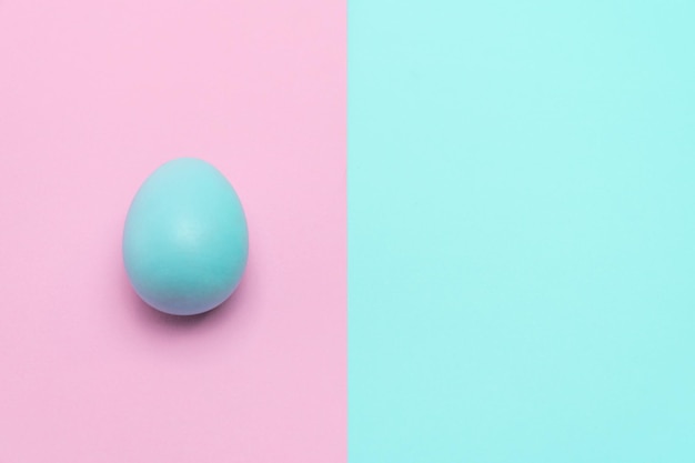 Un huevo de Pascua azul colocado sobre un fondo pastel impactante. En el lado izquierdo de la mesa.