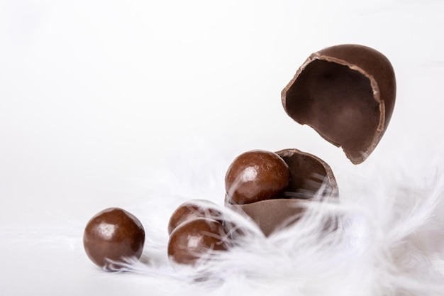 Huevo de pascua de chocolate agrietado con pequeños dulces redondos de chocolate y cáscara de huevo voladora en nido de plumas blancas espacio de copia levitación Golosina de chocolate para niños Concepto de Pascua