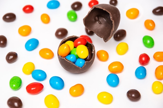 Huevo de Pascua de chocolate roto con decoraciones de caramelos de colores sobre un fondo blanco con caramelos de colores