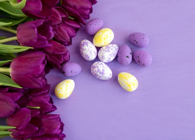 Huevo de Pascua de color y flores de tulipanes morados sobre fondo morado.