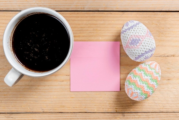 Huevo de pascua colorido con papel de carta vacío y taza de café en una mesa de madera Felices Pascuas