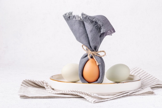 Huevo de Pascua decorado como un conejito en un plato blanco sobre un fondo de hormigón blanco