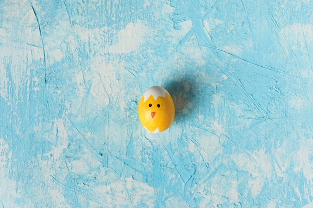 Huevo de Pascua decorado como pollito sobre fondo de textura azul.