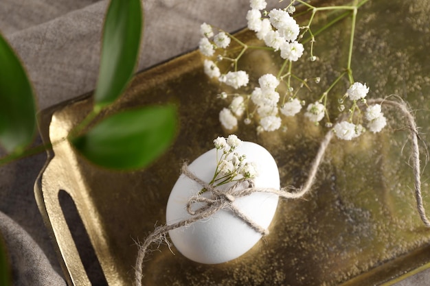 Huevo de Pascua decorado con flores y ramas en bandeja dorada.