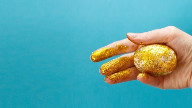 Huevo de Pascua dorado en la mano sobre un fondo azul Fondo de Pascua