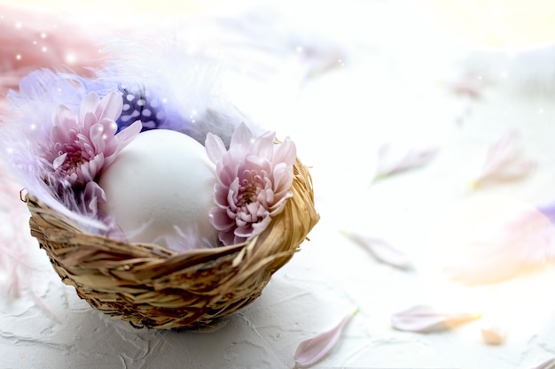 Huevo de Pascua en el nido pequeño con plumas y pétalos de flores sobre un fondo claro huevo de codorniz pintado...